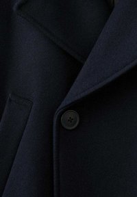 Abrigo de lana azul marino con cuello solapa, bolsillo delantero y un botón redondo de cuatro agujeros. Tejido texturizado, apariencia suave.