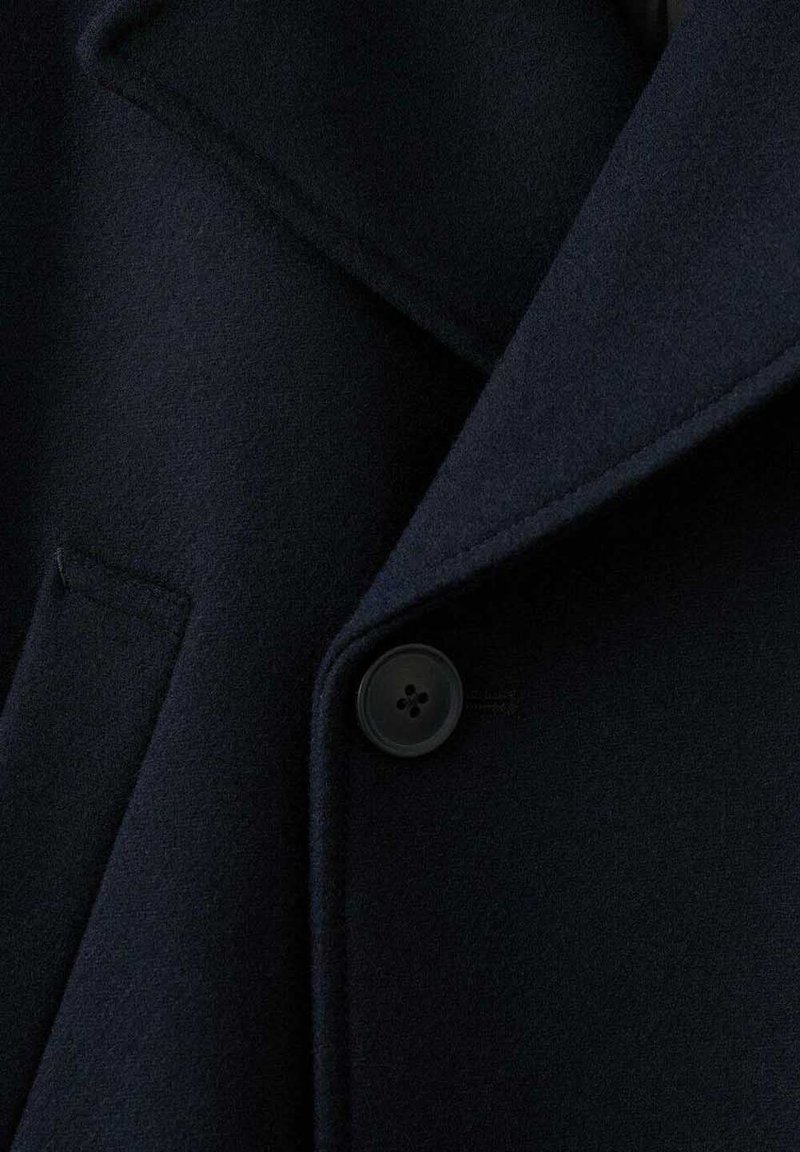 Marineblauer Wollmantel mit Reverskragen, Fronttasche und einem runden, vierlochigen Knopf. Strukturierter Stoff, weiches Aussehen.
