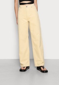 Geel corduroy wijde broek met een textuur, voorzien van voorzakken en een klassieke knoopsluiting, gecombineerd met zwarte plateau sandalen.