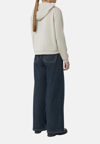 Beige Kapuzenpullover aus weichem Stoff, kombiniert mit weiten dunkelblauen Jeans mit sichtbaren Nähten und großen Taschen.