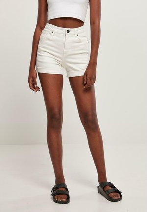 Shorts en denim blanc avec des revers, taille haute et poches avant, associés à des sandales à glissière noires sur un fond neutre.