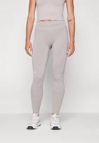 Jasnolavendowe legginsy dopasowane wykonane z elastycznego materiału, z gładką fakturą i logo Under Armour na pasie i łydce.