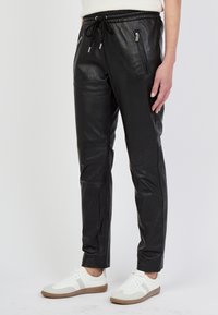 Svarta läderjoggers med en slim fit, som har två dragkedjefickor fram, resårmidja och slät yta. Bärs med vita sneakers.