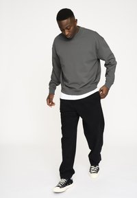 Gray sweatshirt with crew neckline, ribbed cuffs, and waistband. Paired with black pants and black sneakers with white laces.