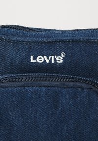 Denim tkanina tamnoplave boje sadrži bijelu izvezenu "Levi's" oznaku i detalj sa zatvaračem duž gornjeg ruba.