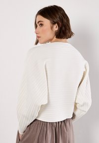 Witte ribgebreide trui met textuurvolle pofmouwen, ronde hals en een aansluitende zoom, gecombineerd met een zachte, vloeiende bruine rok.