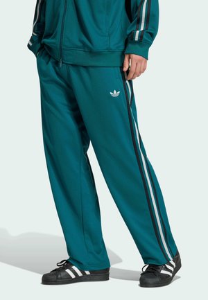 Pantaloni della tuta Adidas color turchese e giacca abbinata con strisce laterali bianche e nere, indossati con sneakers Adidas nere con strisce bianche.