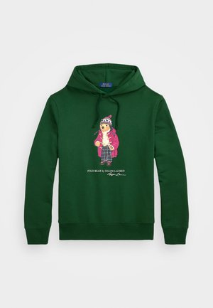 Ciemnozielona bluza z kapturem z grafiką z przodu przedstawiającą niedźwiedzia ubrany w zimowe ubrania oraz tekstem „Polo Bear by Ralph Lauren” poniżej.
