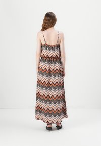 Maxi-jurk met spaghetti-bandjes, voorzien van een zigzagpatroon in oranje, wit en zwart. Geverbonden taille en vloeiende stof.