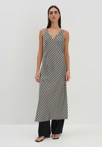 Maxikleid mit schwarz-weißem geometrischem Muster, V-Ausschnitt, dünne Träger, leichtes Material, fließende Silhouette, kombiniert mit weiten schwarzen Hosen.