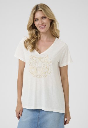 T-shirt blanc en coton avec col en V, présentant un design graphique de lion doré au centre. Manches courtes et coupe légèrement ample.