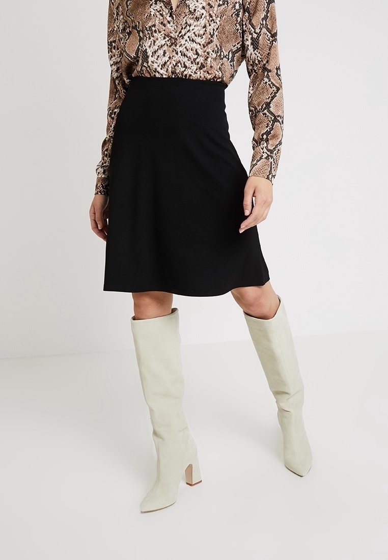 Svart utsvängd kjol i ett mjukt material, tillsammans med knähöga vita stövlar med klack och en slät yta.