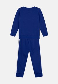 Blaue passende Sweatshirt- und Hosenkombination. Sweatshirt mit langen Ärmeln und Rundhalsausschnitt. Die Hose hat weiße Seitenstreifen und elastische Bündchen.
