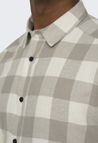 Light gray and white checkered shirt with a button-down collar, featuring navy buttons and a soft, textured fabric.