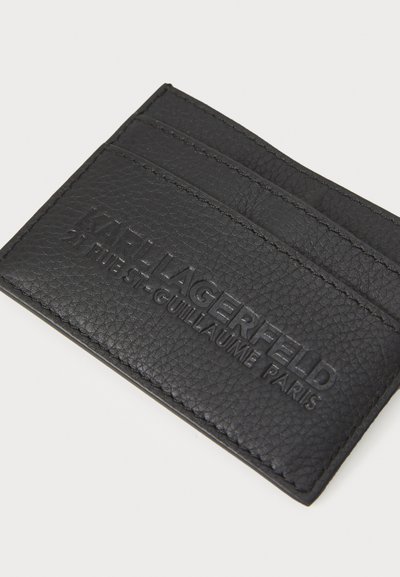 Tarjetero de cuero negro que cuenta con tres ranuras y detalle de logo en relieve. Superficie texturizada con costura a lo largo de los bordes.