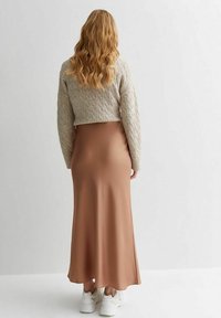 Brun satäng maxi kjol med utsvängd nederkant, kombinerad med en ljusgrå, strukturerad, kort tröja och vita sneakers.