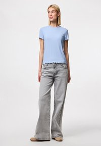 T-shirt bleu clair à côtes avec manches courtes à bord festonné et un ourlet court, associé à un jean évasé gris délavé taille haute.