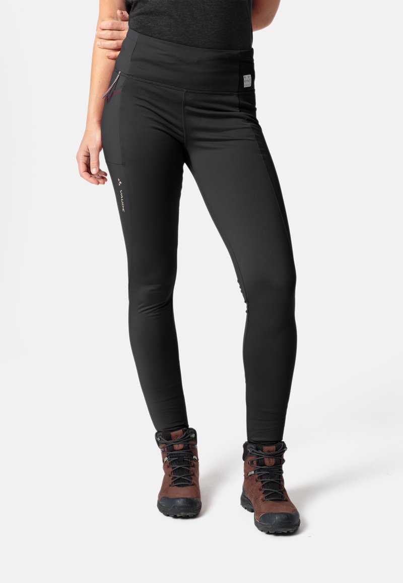 Schwarze Stretch-Leggings mit hohem Bund, seitlichem Reißverschlusstaschen und figurbetontem Schnitt. Kombiniert mit braunen Wanderschuhen für den Einsatz im Freien.
