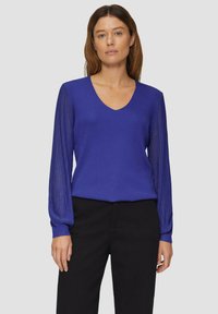 V-hals pullovertrui in levendig blauw, met textuur ribgebreide mouwen. Materiaal lijkt lichtgewicht, aansluitend op het lichaam met lange mouwen.