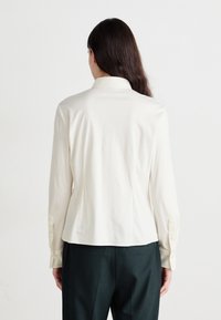 Cremefarbige Langarmbluse mit taillierter Silhouette, weichem Textil und klassischem Kragen; mit Knopfärmeln und einem schlichten Design ausgestattet.