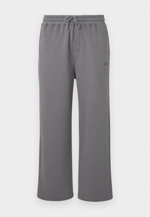 Grå vide bukser i sweatsmateriale med elastisk talje og snørebånd, med sidelommer og diskret broderi på venstre lår.