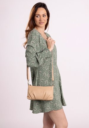 Beige Leder-Umhängetasche mit weichem, gerafftem Design und abnehmbarem Riemen; kombiniert mit einem grünen, floral gemusterten Kleid.