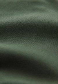 Gros plan sur un tissu vert foncé lisse avec une fine texture côtelée diagonale et de doux plis créant des ombres légères.
