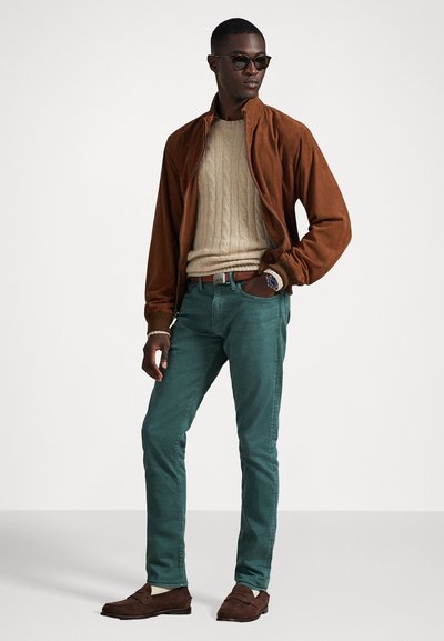 Brūns zamšs bomberis, krēmkrāsas adīts džemperis, tirkīza bikses, brūnas loafer kurpes, tumši saulesbrilles un rokas pulkstenis. Vienkāršs, teksturēts dizains.