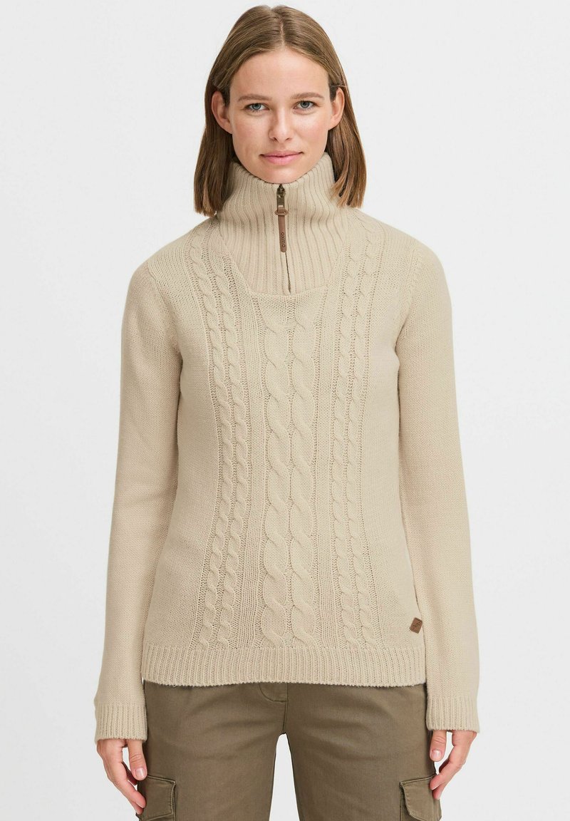 Beige Strickpullover mit hohem Kragen, halbem Reißverschluss, gerippten Bündchen und Saum. Weiche Textur; besitzt ein Etikett auf der linken Seite.