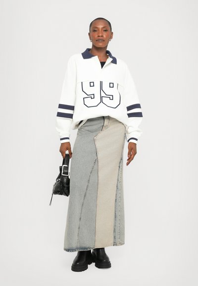 White sweatshirt with navy accents and "99" print, paired with a patchwork denim maxi skirt in light and dark tones. Black platform boots.