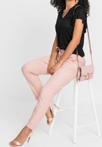 Black v-neck t-shirt with ruffled sleeves, paired with light pink tapered pants, and a blush crossbody bag featuring a circular accent.