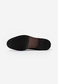 Suela de zapato negra con un acabado liso, fondo de goma texturizada y un acento marrón a lo largo del borde. Diseño plano, sin logotipos ni patrones visibles.
