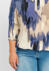 Blusa multicolore caratterizzata da un motivo astratto in tonalità di blu, crema e nero. Ha un collo tondo e maniche a tre quarti.