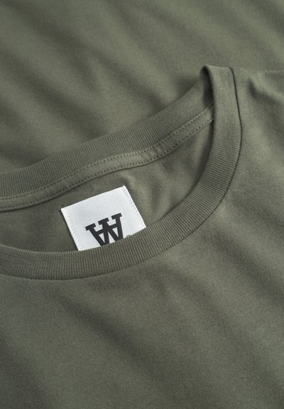 Λαδί πράσινο T-shirt με στρογγυλή λαιμόκοψη και λευκή ορθογώνια ετικέτα που έχει ραμμένο στο εσωτερικό του γιακά ένα μαύρο στυλιζαρισμένο λογότυπο "W".