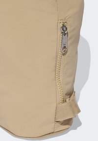 Bolsa de nylon beige con cremallera visible, tejido texturizado y una correa lateral para cierre seguro. Diseño minimalista con detalles prácticos.