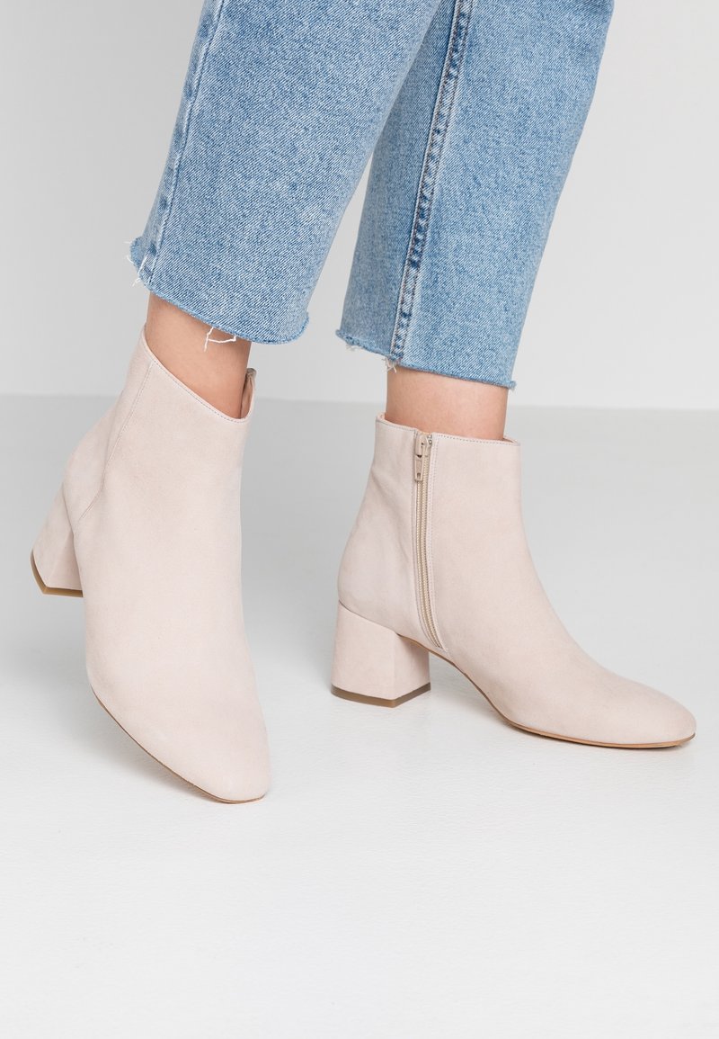 Bottines en daim beige clair avec talons blocs et fermetures éclair latérales, portées avec un jean denim bleu clair raccourci.