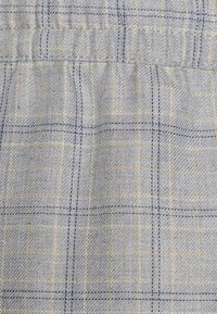 Tessuto grigio chiaro con un motivo a griglia caratterizzato da linee blu e gialle. Il materiale sembra avere una texture con una finitura liscia. Dettaglio della vita regolabile.