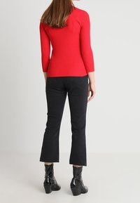 Czerwona prążkowana bluzka z długim rękawem zestawiona z czarnymi dzwonowatymi jeansami i czarnymi botkami za kostkę. Strój ma dopasowany krój i teksturowaną tkaninę.
