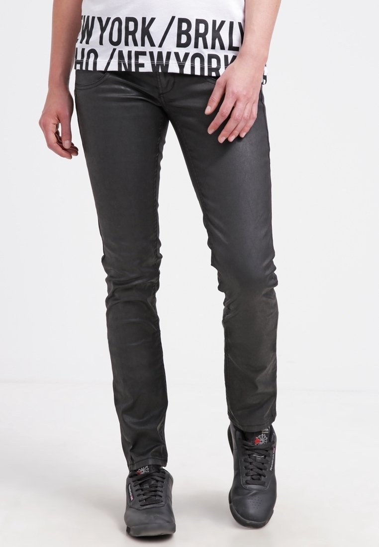 Černé skinny džíny s koženým vzhledem a hladkou texturou; mají pět kapes a pohodlně sedí v pase, spárované se šedými teniskami.