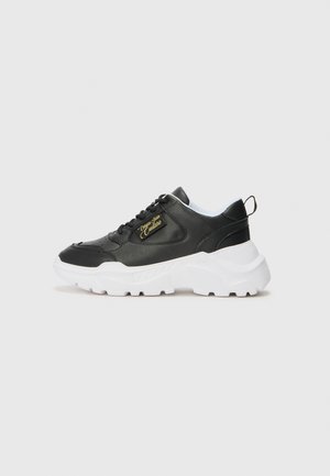 Sneaker in pelle nera con suola in gomma bianca, dotata di collo imbottito, chiusura con lacci e dettaglio del logo dorato sul lato.