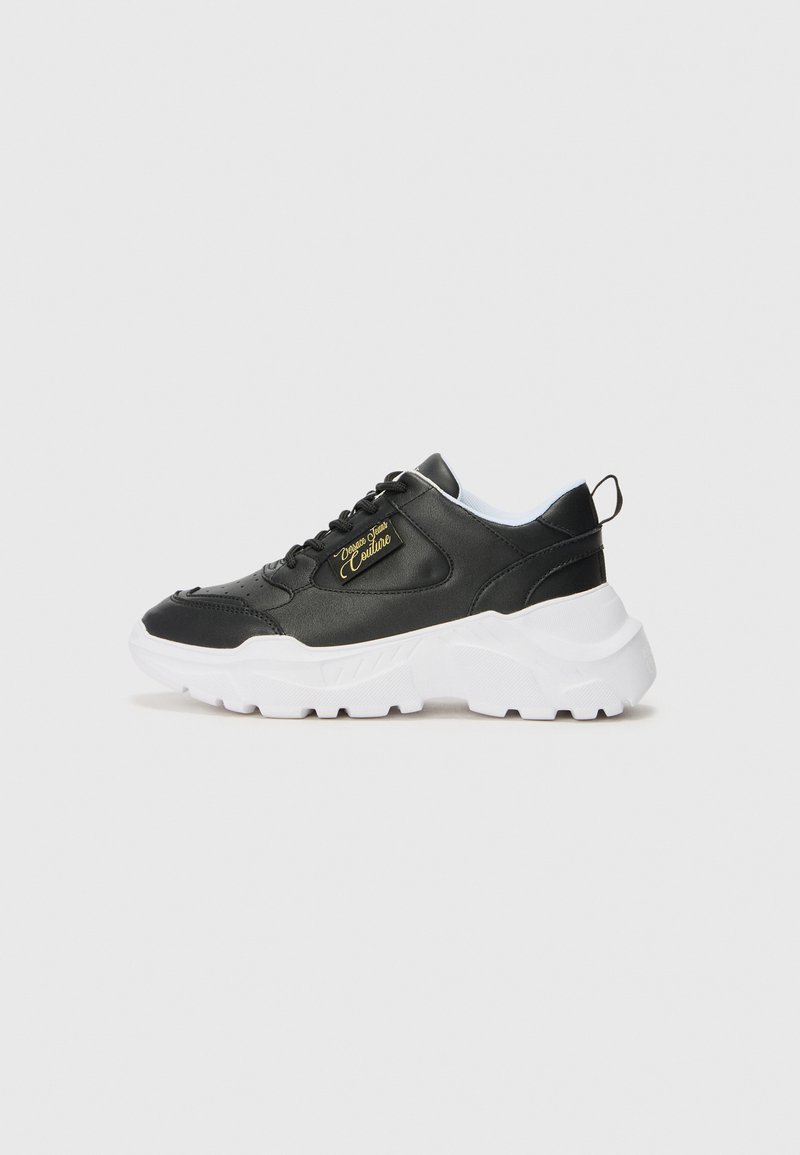 Must musta sneaker valge kummist tallaga, millel on pehmendatud kaelus, paeltega esiosa ja külgedel kuldne logo detail.