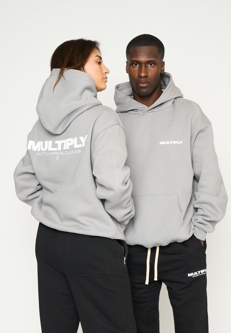 Šedé mikiny s prednými vreckami majú na zadnej strane veľké biele logo "MULTIPLY". Modely majú na sebe čierne tepláky s minimálnym zdobením.