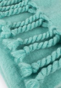 Un tissu bleu clair doux et texturé avec des accents de corde torsadée aux extrémités en pompon, créant un détail de design unique.