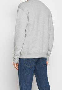 Grå sweatshirt med rund halsringning, ribbade ärmslut och nederkant, tillsammans med mörkblå denimjeans med en klassisk femfickorsdesign.