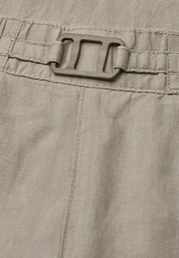 Gros plan d'un tissu beige avec une boucle rectangulaire en plastique attachée à des passants de ceinture cousus, montrant la texture et les détails du matériau.