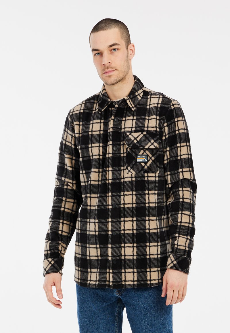 Camisa de franela a cuadros en negro y beige con un bolsillo en el pecho y etiqueta de la marca. Presenta un cierre frontal de botones y mangas largas.