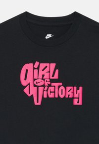 Μαύρη βαμβακερή μπλούζα T-shirt με έντονη ροζ γραφική εκτύπωση που γράφει "Κορίτσι της Νίκης". Στρογγυλή λαιμόκοψη και κοντά μανίκια.