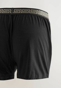 Schwarze Boxer Shorts mit glatter Textur. Verfügt über einen elastischen Bund in Beige mit einem geometrischen Design. Keine Taschen.