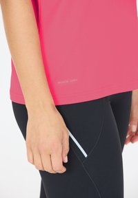 Rosa snabb-torkande träningsskjorta med en slät textur, kombinerad med svarta leggings med en vit sidostripe.