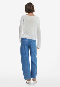 Maglione bianco a maglia testurizzata con scollatura a barca; abbinato a jeans ampi a vita alta di un leggero blu con tasche posteriori.